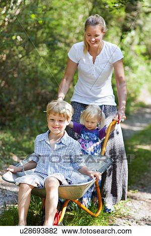 Stock Image - Mother pushing children in wheelbarrow. Fotosearch
