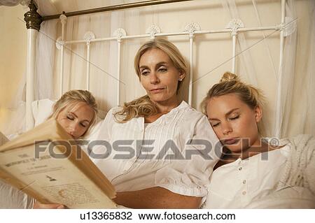 Stock Image - Mother reading to sleeping daughters. Fotosearch