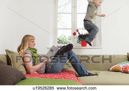 Mother relaxing as son jumps on sofa View Large Photo Image Stock Photography - Mother relaxing as son jumps on sofa. Fotosearch