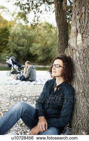 Stock Photograph - Mother resting by tree away from family. Fotosearch