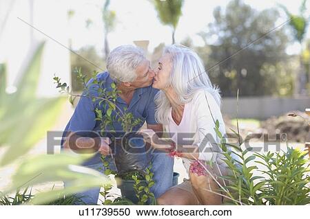 Stock Image - Older couple kissing in garden. Fotosearch