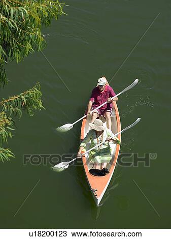 Stock Image - Older couple rowing canoe on lake. Fotosearch