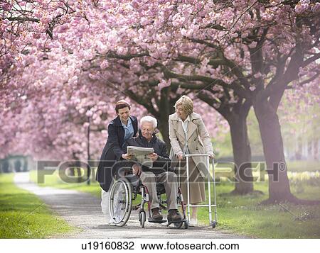 Stock Image - Older couple with caretaker in park. Fotosearch