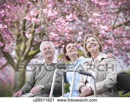 Stock Image - Older couple with caretaker in park. Fotosearch