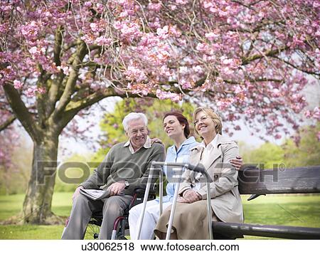 Stock Photo - Older couple with caretaker in park. Fotosearch