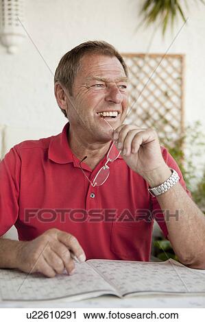 Stock Image - Older man completing crossword puzzle. Fotosearch