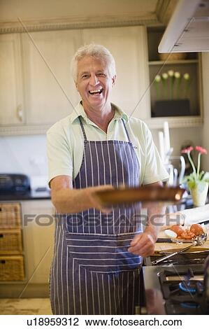 Stock Image - Older man cooking in kitchen. Fotosearch