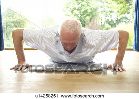Stock Image - Older man doing pushups indoors. Fotosearch