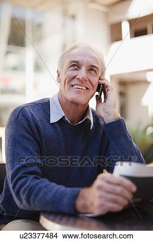 Picture - Older man on cell phone at cafe. Fotosearch