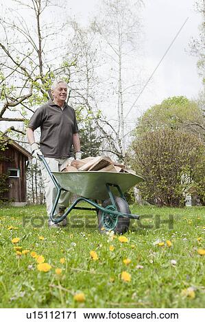 Stock Image - Older man pushing wheelbarrow. Fotosearch