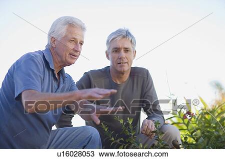 Stock Image - Older men examining garden together. Fotosearch