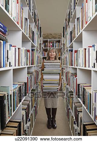 Stock Image - Older woman carrying books in library. Fotosearch