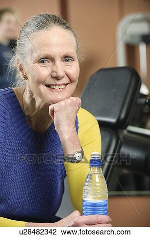 Stock Image - Older woman drinking water in gym. Fotosearch