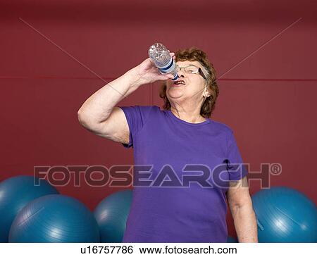 Stock Photograph - Older woman drinking water in gym. Fotosearch