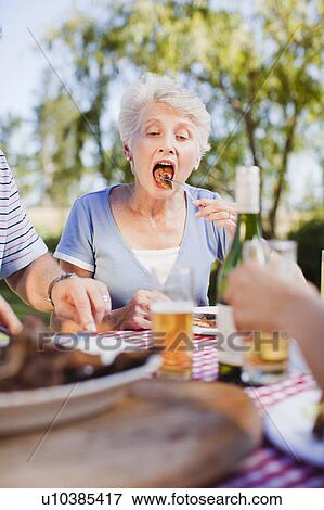 Older woman eating at picnic table View Large Photo Image Stock Photo - Older woman eating at picnic table. Fotosearch