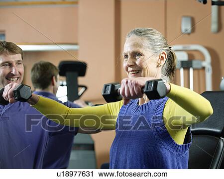 Stock Image - Older woman lifting weights in gym. Fotosearch