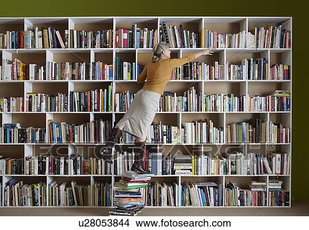 Picture - Older woman standing on stack of books. Fotosearch