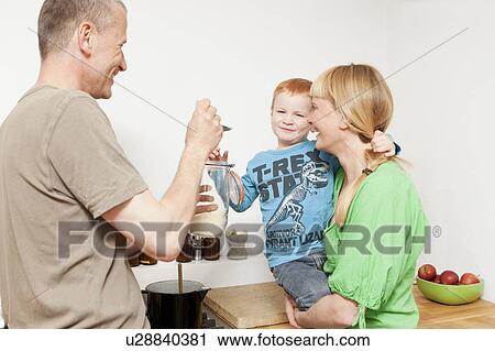 Parents feeding reluctant son in kitchen View Large Photo Image Stock Image - Parents feeding reluctant son in kitchen. Fotosearch