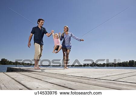 Parents swinging daughter on dock View Large Photo Image Stock Photograph - Parents swinging daughter on dock. Fotosearch