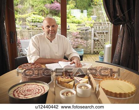 Stock Image - Pastry chef with cakes at dining table. Fotosearch