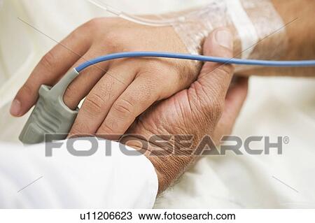 Stock Image - Person holding hospital patient’s hand. Fotosearch