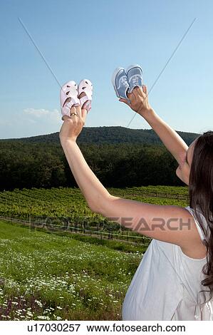 Stock Photo - Pregnant woman examining baby shoes. Fotosearch