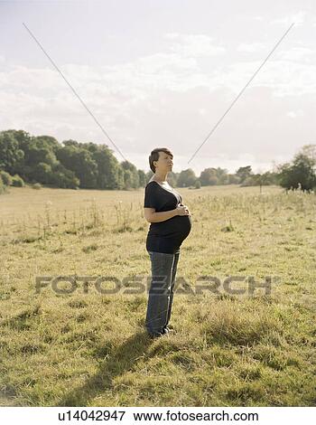 Pregnant woman standing in field View Large Photo Image Stock Photo - Pregnant woman standing in field. Fotosearch