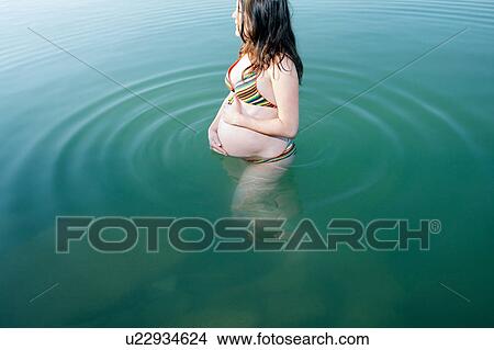 Picture - Pregnant woman standing in lake. Fotosearch