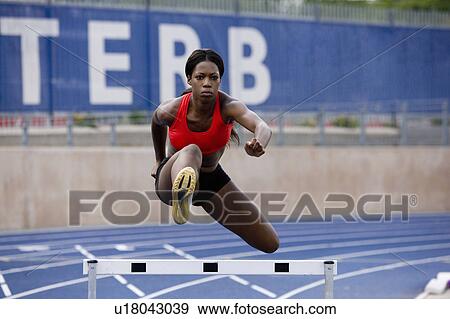 Runner jumping over hurdles on track View Large Photo Image Stock Photo - Runner jumping over hurdles on track. Fotosearch