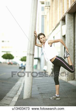 Stock Image - Runner stretching against pole. Fotosearch