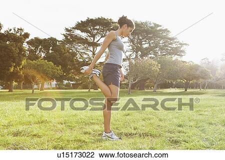 Stock Image - Runner stretching in field. Fotosearch