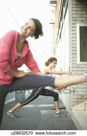 Stock Image - Runners stretching against wall. Fotosearch