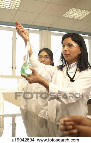 Picture - Scientist adding solution to beaker. Fotosearch