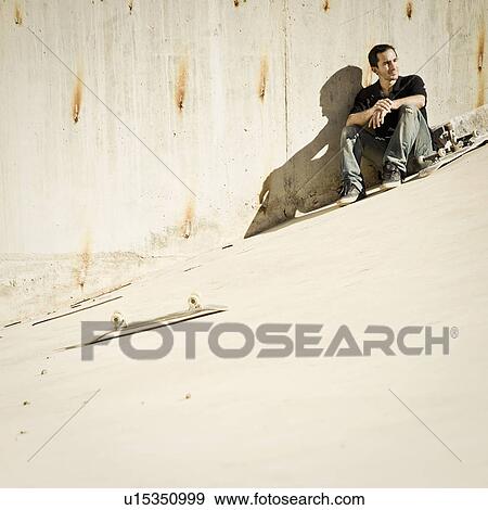 Stock Photo - Skateboarder sitting on concrete slope. Fotosearch