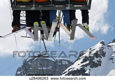Stock Image - Skiers riding chair lift over mountains. Fotosearch