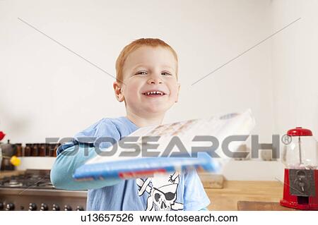 Smiling boy holding book in kitchen View Large Photo Image Stock Photograph - Smiling boy holding book in kitchen. Fotosearch