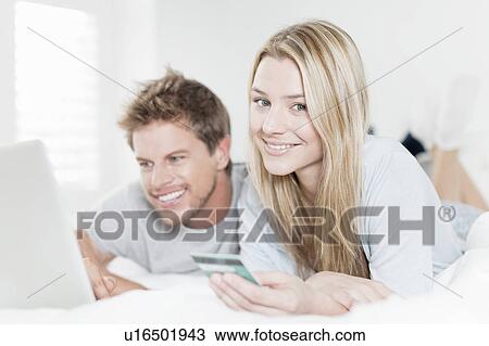Smiling couple shopping online in bed View Large Photo Image Stock Image - Smiling couple shopping online in bed. Fotosearch