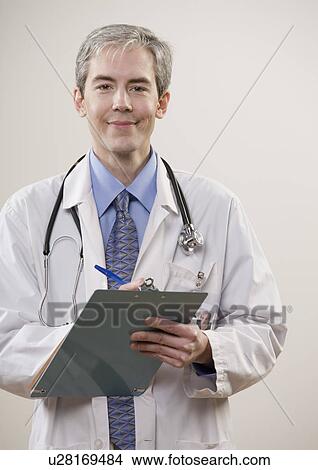 Smiling doctor writing on clipboard View Large Photo Image Picture - Smiling doctor writing on clipboard. Fotosearch