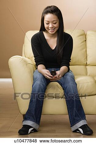 Smiling girl using cell phone on couch View Large Photo Image Stock Photo - Smiling girl using cell phone on couch. Fotosearch