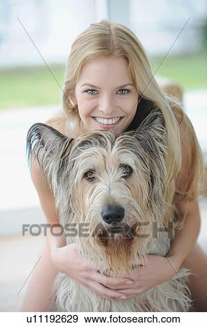 Stock Photo - Smiling woman hugging dog at home. Fotosearch