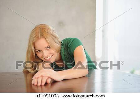 Stock Image - Smiling woman laying on table. Fotosearch