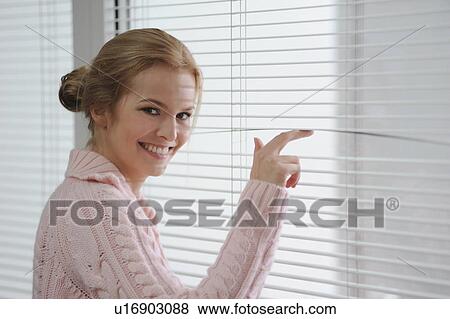 Stock Photo - Smiling woman looking through blinds. Fotosearch