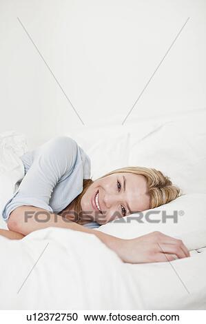 Stock Image - Smiling woman relaxing in bed. Fotosearch