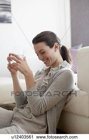 Stock Image - Smiling woman sitting by couch. Fotosearch