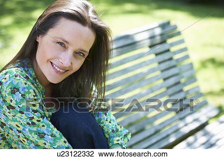 Smiling woman sitting on park bench View Large Photo Image Stock Image - Smiling woman sitting on park bench. Fotosearch