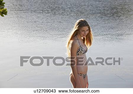 Stock Image - Smiling woman wearing bikini by water. Fotosearch