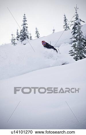 Stock Image - Snowboarder riding down mountainside. Fotosearch