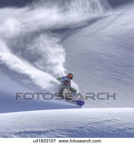 Stock Photo - Snowboarder riding down mountainside. Fotosearch