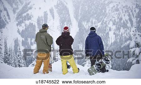Stock Image - Snowboarders admiring mountainside. Fotosearch