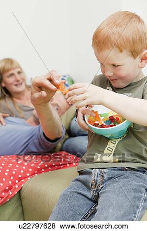 Son sharing candies with father on sofa View Large Photo Image Stock Photo - Son sharing candies with father on sofa. Fotosearch